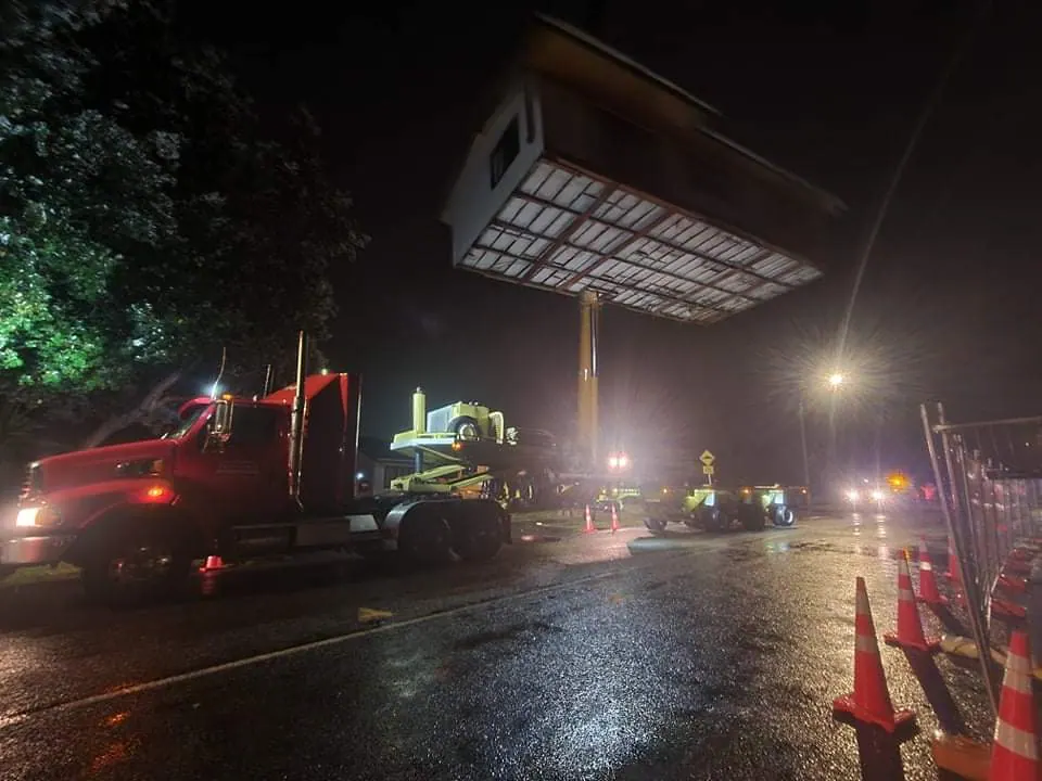 Night crane lift hoisting house section over road and obstacles